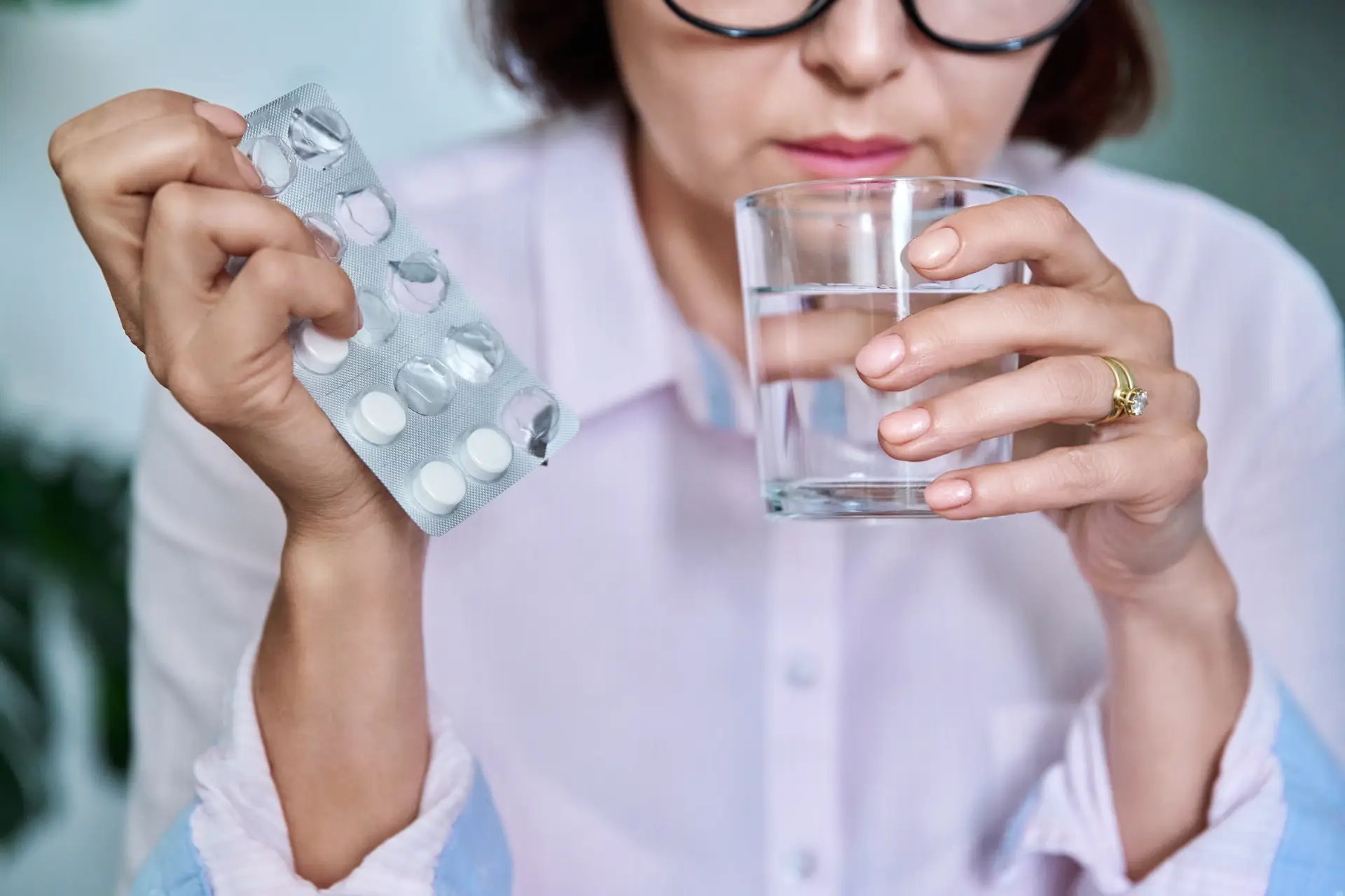 Close-up of womans hand with blister of pills and glass of water