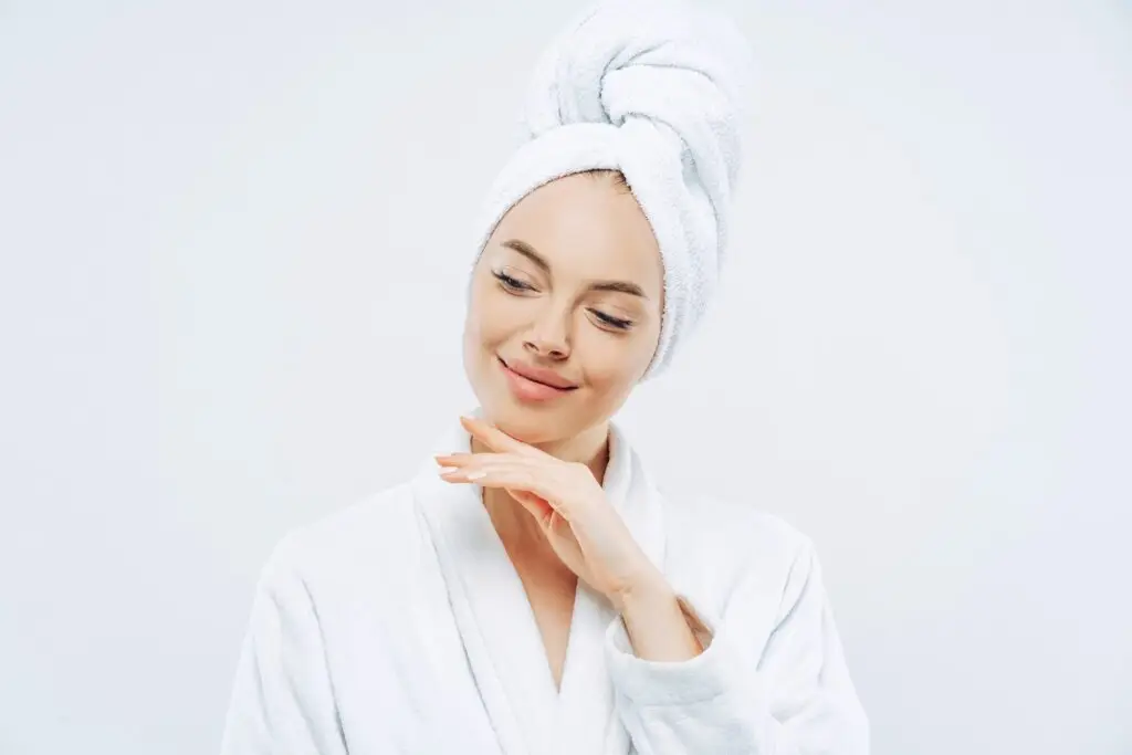 Natural woman touches jawline, towel on head, dries hair, cares for body, clean skin